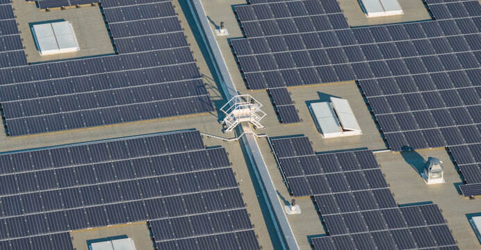 Aerial view of a large rooftop photovoltaic installation integrated around skylights and technical infrastructure on a commercial building in Livron-sur-Drome, Auvergne-Rhone-Alpes, France.