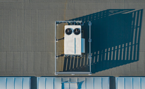 Aerial view of a rooftop HVAC cooling unit casting a geometric shadow across the roof of a modern industrial building in Livron-sur-Drome, Auvergne-Rhone-Alpes, France.