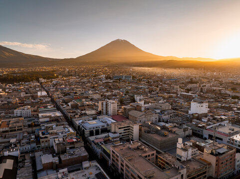 Aerial view of the city of Arequipa at sunset with the Misti volcano in the background, featuring dense urban rooftops and golden light over Arequipa, Arequipa, Peru.