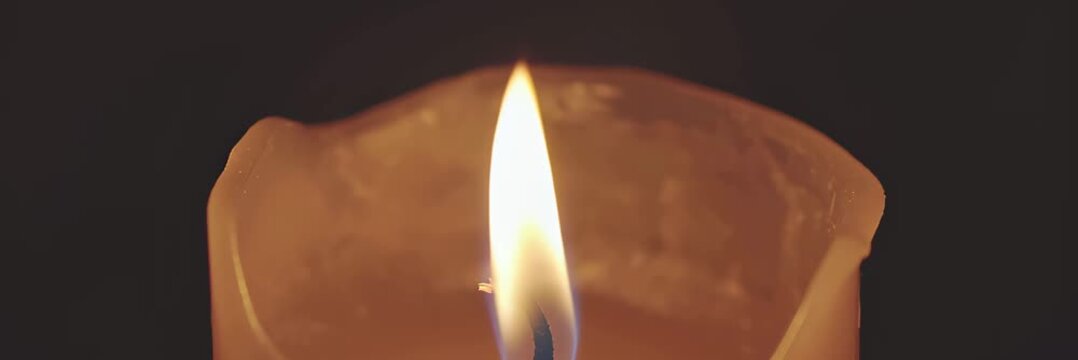 Single candle flame glowing in darkness, calm memorial concept, website banner with copy space for text