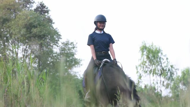 Asian female equestrian athletes coaches wearing helmets practical attire practice outdoor training ground jogging slowly across the grass evening familiarizing themselves horses  graceful movements.