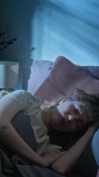 Vertical of Caucasian young woman sleeping in bed at night with shadows moving across her face. Footage perfect for sleep health, insomnia awareness, or bedding commercials