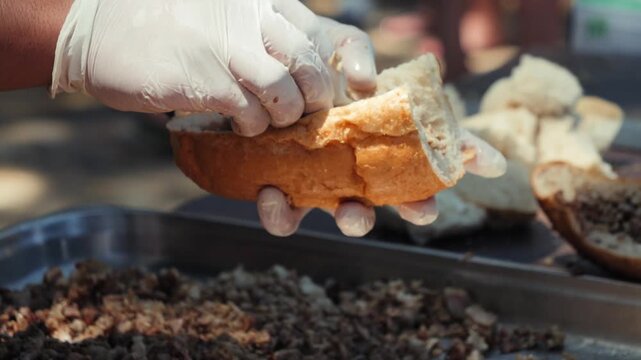 Chef preparing traditional Turkish kokorec by filling a fresh bread roll with finely chopped seasoned lamb intestines. High quality 4k footage