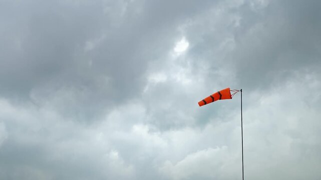 An orange with reflection stripe windsock on cloudy sky before storm coming weather. The equipment using to indication windy speed and direction.