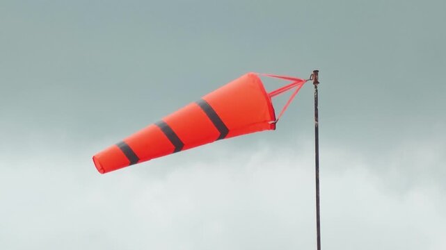 An orange with reflection stripe windsock on cloudy sky before storm coming weather. The equipment using to indication windy speed and direction.