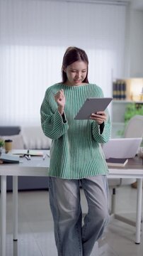 Young Asian woman using digital tablet for online education and studying in modern bright home workspace