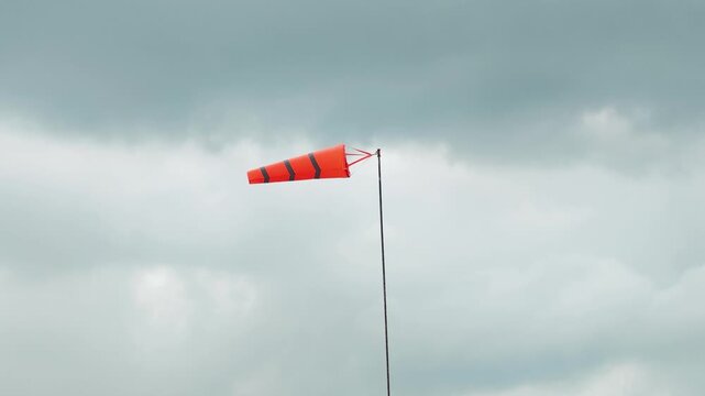 An orange with reflection stripe windsock on cloudy sky before storm coming weather. The equipment using to indication windy speed and direction.