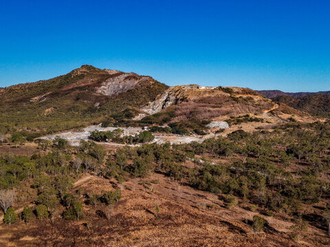 Aerial view of the Manton Quarry Road site featuring an open-pit quarry surrounded by dry eucalyptus forest and rocky hills under a clear blue sky in Calcium, Queensland, Australia.