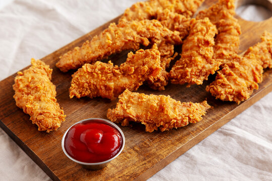 Organic Crispy Chicken Strips with Ketchup on a Wooden Board, side view.