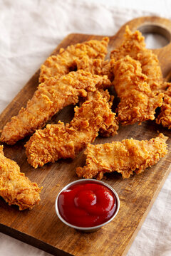 Organic Crispy Chicken Strips with Ketchup on a Wooden Board, side view.