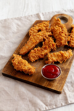 Organic Crispy Chicken Strips with Ketchup on a Wooden Board, side view.