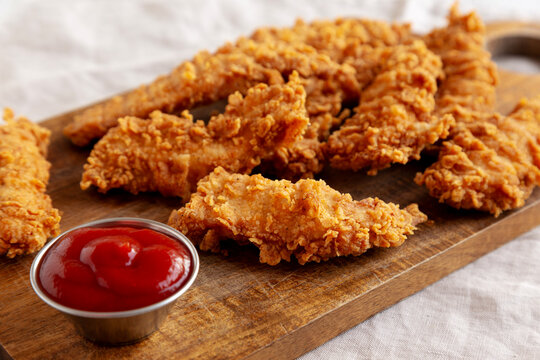 Organic Crispy Chicken Strips with Ketchup on a Wooden Board, side view.