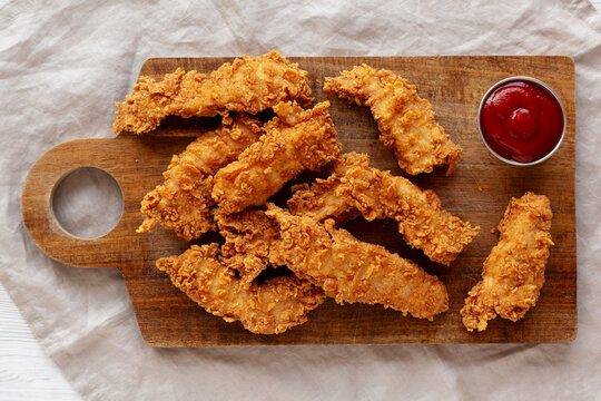 Organic Crispy Chicken Strips with Ketchup on a Wooden Board, top view.