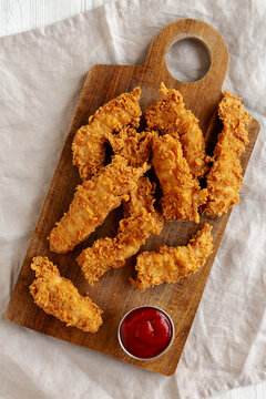 Organic Crispy Chicken Strips with Ketchup on a Wooden Board, top view.