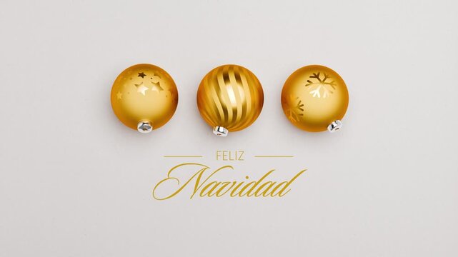 Three golden christmas baubles spinning on a paper surface. Spanish language Merry Christmas messages (Feliz Navidad) appearing and dissolving. Loopable video