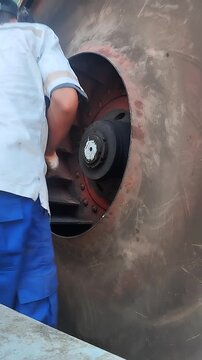Industrial technician inspects large ventilation fan impeller during machinery maintenance service in factory