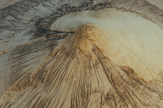 Aerial view of sand piles illuminated by warm sunlight, featuring intricate textures and erosion patterns in the landscape of Poland.