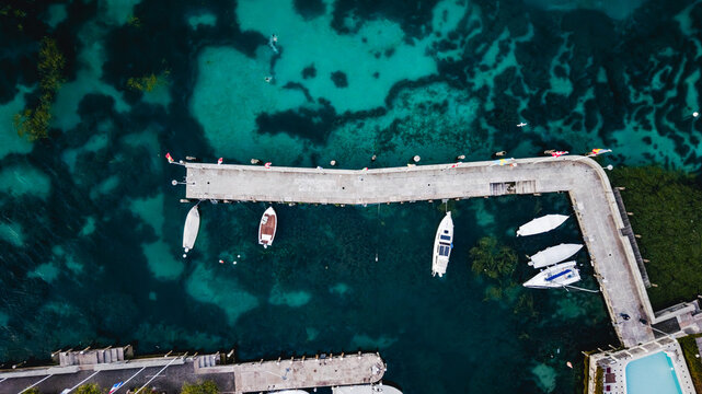 Aerial view of a stone pier extending into the turquoise waters of Lake Garda with moored boats in Sirmione, Lombardy, Italy.