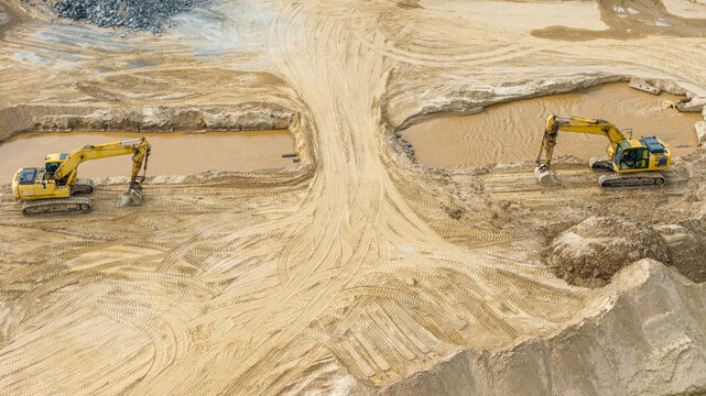 Aerial view of a large sand and gravel mine with two yellow excavators working near muddy water pools and tire tracks in Poland.