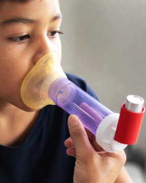 Boy using metered dose inhaler with spacer for asthma treatment