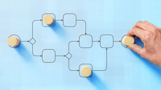 Hand placing a wooden token onto a drawn process flowchart on a blue background. Business process management, workflow optimization, and planning concept