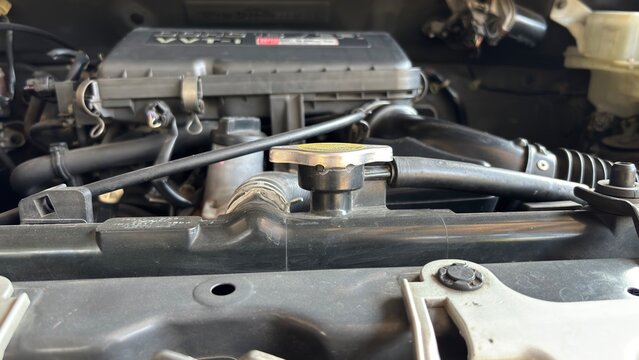 Detailed view of automobile radiator cap with yellow caution label, hoses, clamps, and engine block. Represents automotive maintenance, diagnostics, and mechanical engineering.