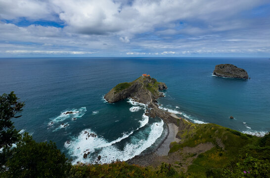 serene and dramatic aerial view of a rocky coastline with a small island and lighthouse, surrounded by lush green grass and blue ocean waters, travel and nature scenes.