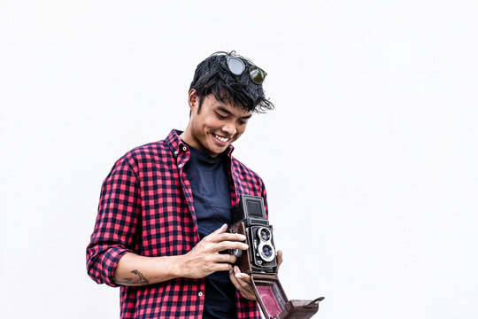 Smiling gen z photographer adjusts a vintage twin lens reflex camera against a clean white wall with generous copy space. Minimal portrait highlights analog creativity and retro technology.