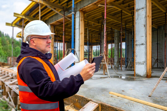 Construction Supervision. Site engineer checks building formwork and concrete structure using tablet and blueprints during construction quality inspection.