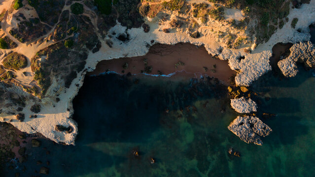 serene aerial view of secluded sandy beach with rocky shoreline and lush vegetation under a bright blue sky, looking down from above on a tranquil coastal landscape. Praia dos Aveiros Portugal