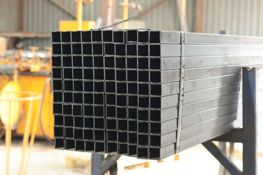 Close-up of stacked square steel hollow section profiles with visible cut ends inside an industrial metal workshop.