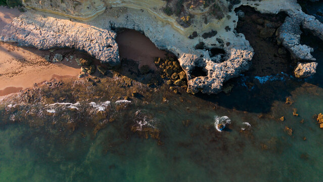 serene rock formations on a sandy beach with ocean waves and sedimentary rock under an aerial view of a coastal landscape in brown and gray tones, nature photography and travel. Praia dos Aveiros 