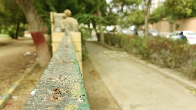 Close up shallow depth of field shot of an old green metal park fence rail with a heavily blurred walkway and background