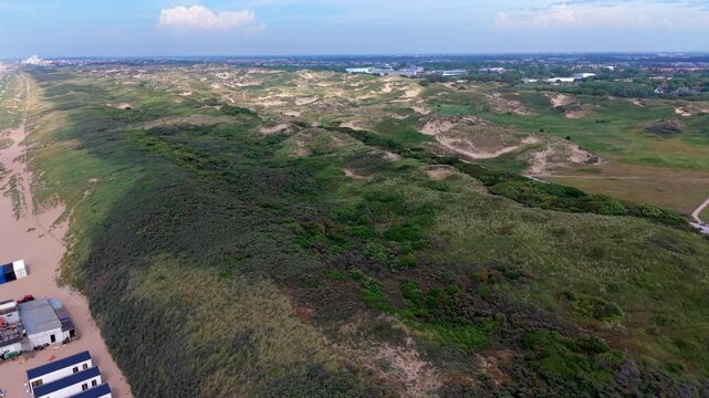 Aerial view video clip of rolling coastal sand dunes, marram grass vegetation, beach cabins, and North Sea shoreline in Katwijk aan Zee, South Holland, Netherlands on a sunny day