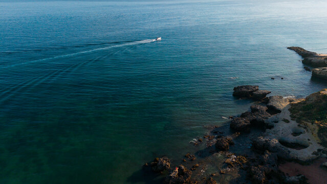 sailing speedboat across rocky coastal landscape with clear blue sea aerial view adventure tranquility natural beauty outdoor pursuit travel vacation water rock blue green clean background.