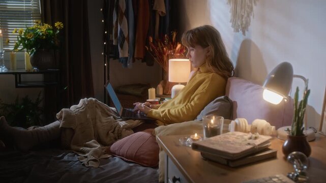 Caucasian young woman lying in bed, typing on laptop computer at night. Footage suitable for remote work, online education, or freelance lifestyle marketing