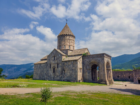 Historic Armenian Tatev monastery stands on grassy hillside near mountains