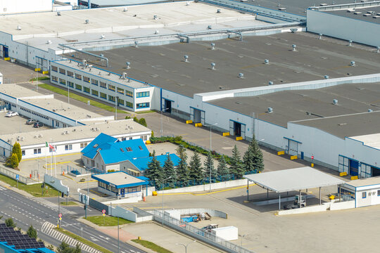 Aerial view of a tissue paper reels production facility featuring large industrial buildings with white walls and blue roofs, surrounded by parking areas and access roads in Poland.