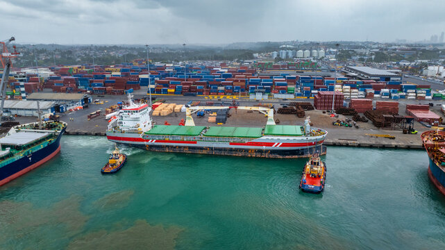Aerial view of the Port of Haina with a cargo ship being maneuvered by tugboats near the container terminal in Bajos de Haina, San Cristobal Province, Dominican Republic.
