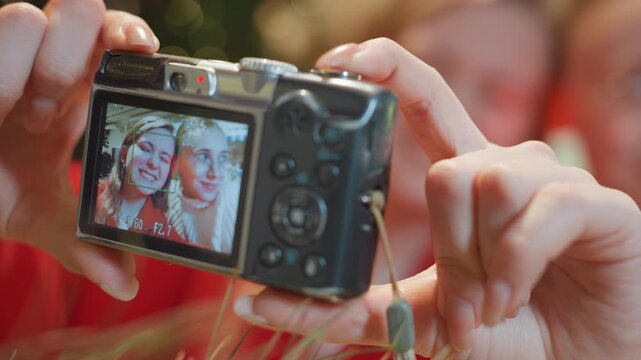 Closeup hands holding camera in cafe, compact digital display shows two smiling friends reviewing selfie, warm bokeh lights, cozy atmosphere, casual clothing, fingers adjusting settings and pressing
