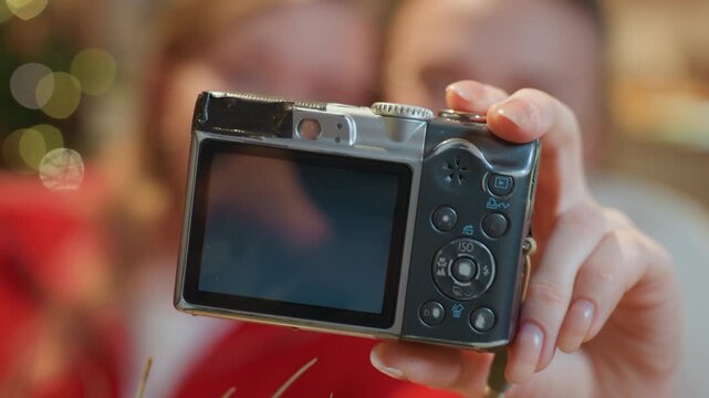 Closeup caucasian women in cafe reviewing camera screen, selfie preview on display with hands gripping compact digital camera, buttons and playback visible, vloggers checking composition, warm bokeh