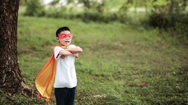 Cute Asian Little Boy in Superhero Costume Arms Crossed Standing Confidently for Child Imagination Concept in Park