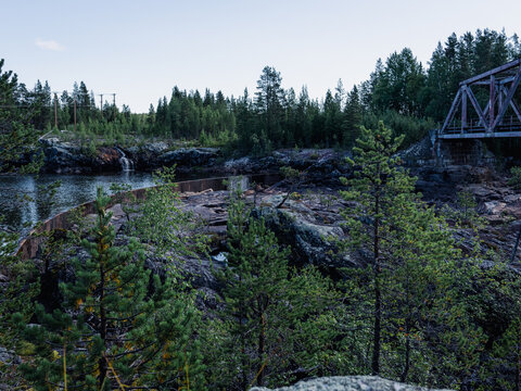Rocky river landscape with a small waterfall, forest vegetation and an old railway bridge in northern Sweden.