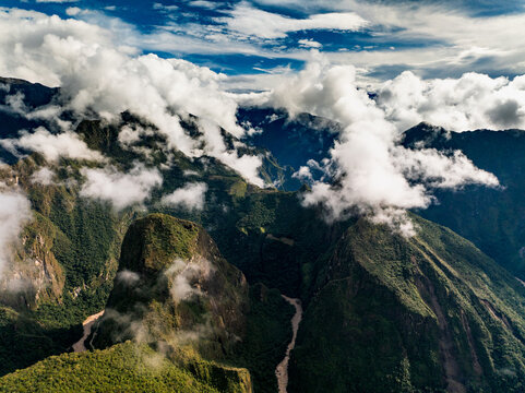 Aerial view of the Historic Sanctuary of Machu Picchu and the winding Urubamba River surrounded by lush Andean mountains and dramatic clouds in Urubamba Province, Cusco, Peru.