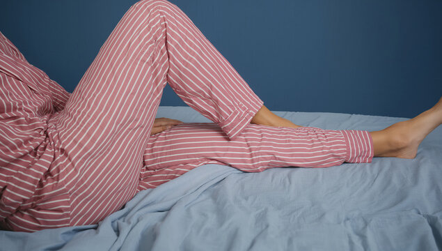 Person in striped pajamas relaxing on a bed with blue sheets and wall