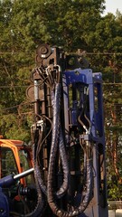Niebieska wiertnica gąsienicowa z hydraulicznym osprzętem stoi na placu budowy. W tle widać las, kontenery oraz elementy betonowe. Maszyna jest przygotowana do specjalistycznych prac ziemnych. © tomo81