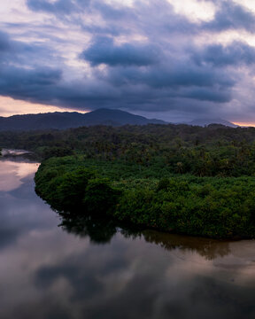 Aerial view of Parque Nacional Natural Tayrona featuring a winding river flowing through lush tropical forest under a dramatic cloudy sunset sky in Magdalena, Colombia.