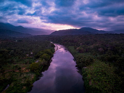 Aerial view of Parque Nacional Natural Tayrona with a river winding through dense tropical forest under a purple sunset sky in Magdalena, Colombia.