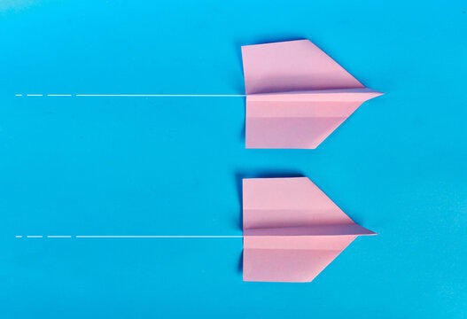Two pink paper airplanes flying on parallel white paths on blue background
