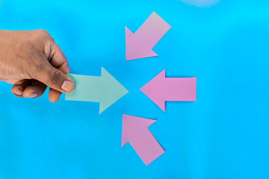 Hand holding green right arrow against three pink arrows pointing opposite on blue background
